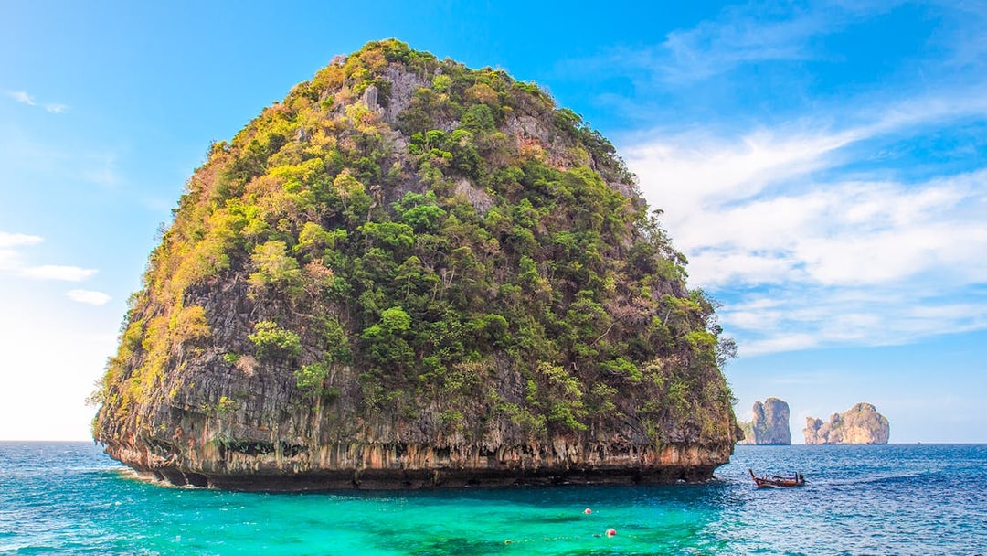 Limestone cliff and turquoise water at Loh Samah Bay, Krabi, with a traditional boat nearby.