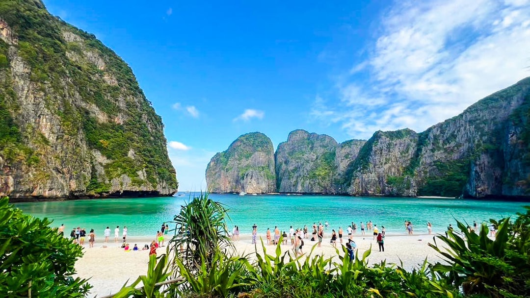 Tourists enjoying the beach at Maya Bay, Krabi, with limestone cliffs in the background.