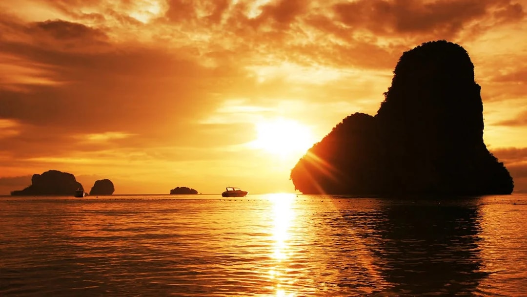Sunset over limestone cliffs and boat in Krabi, Thailand.