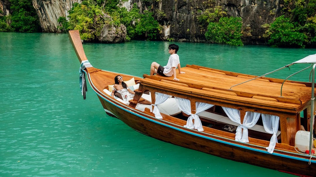 Longtail boat on turquoise water in Krabi with two people relaxing on deck.