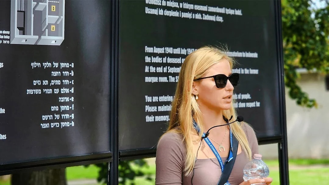 Guide explaining Auschwitz Birkenau history during a tour, standing near informational boards.