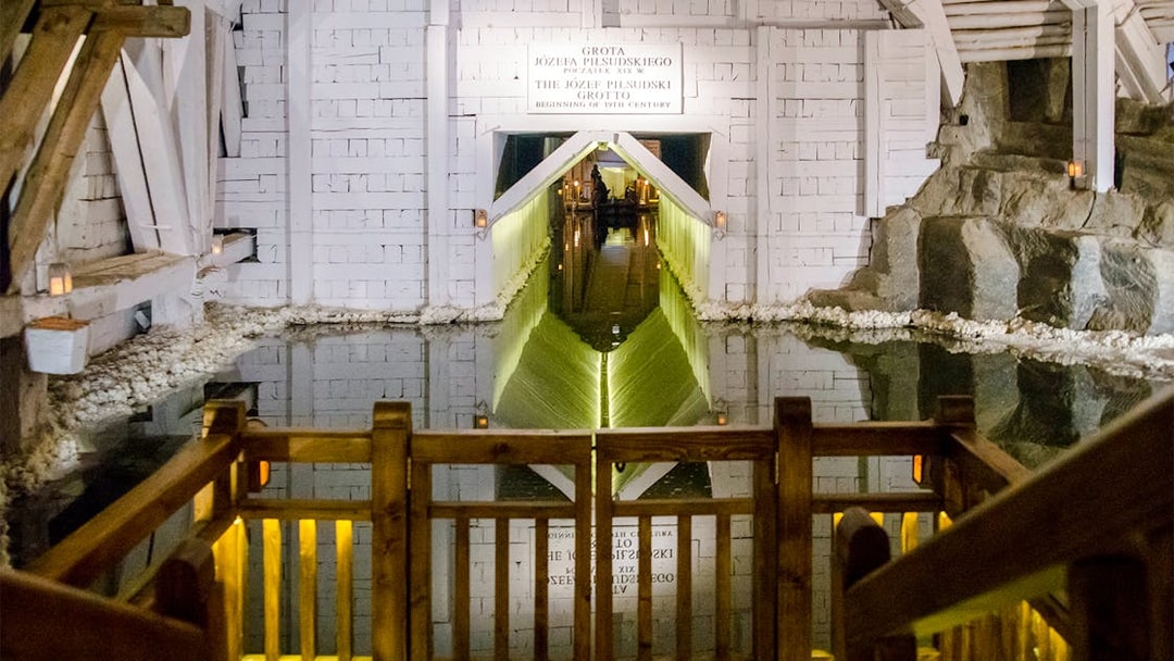 Wieliczka Salt Mine salt lake with wooden railing and illuminated tunnel entrance.