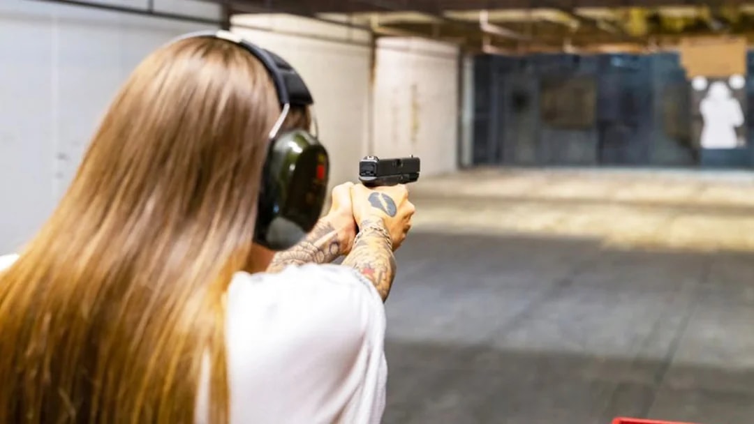 Person aiming a handgun at a target in an indoor shooting range.