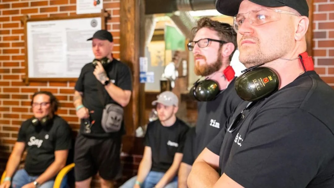 Group of people at an indoor shooting range with ear protection, part of an extreme shooting tour.