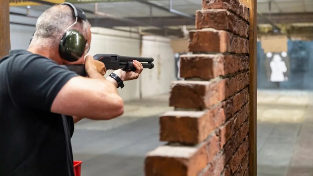 Man aiming shotgun at target in indoor shooting range.