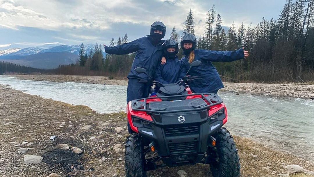 Visitors on a quad bike by a river in Zakopane, Poland, with mountains in the background.