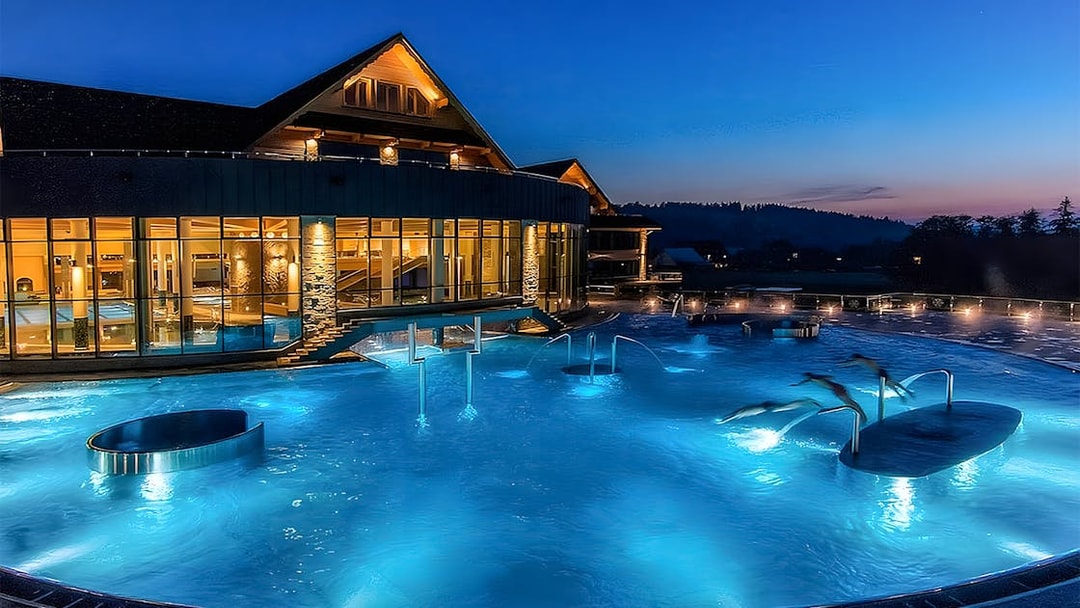 Zakopane Thermal Baths outdoor pool illuminated at night with scenic mountain backdrop.