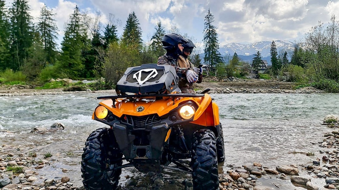Visitors riding a quad bike by a river in Zakopane with mountains in the background.