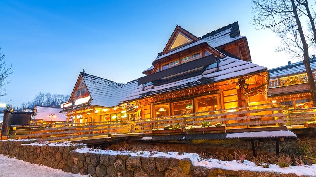 Wooden chalet in Zakopane with snow-covered roof and warm lights at dusk.