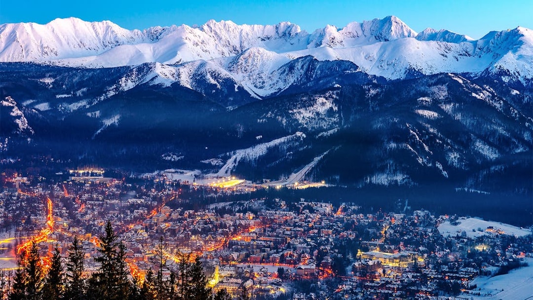 Zakopane cityscape with illuminated streets and snow-covered Tatra Mountains in the background.