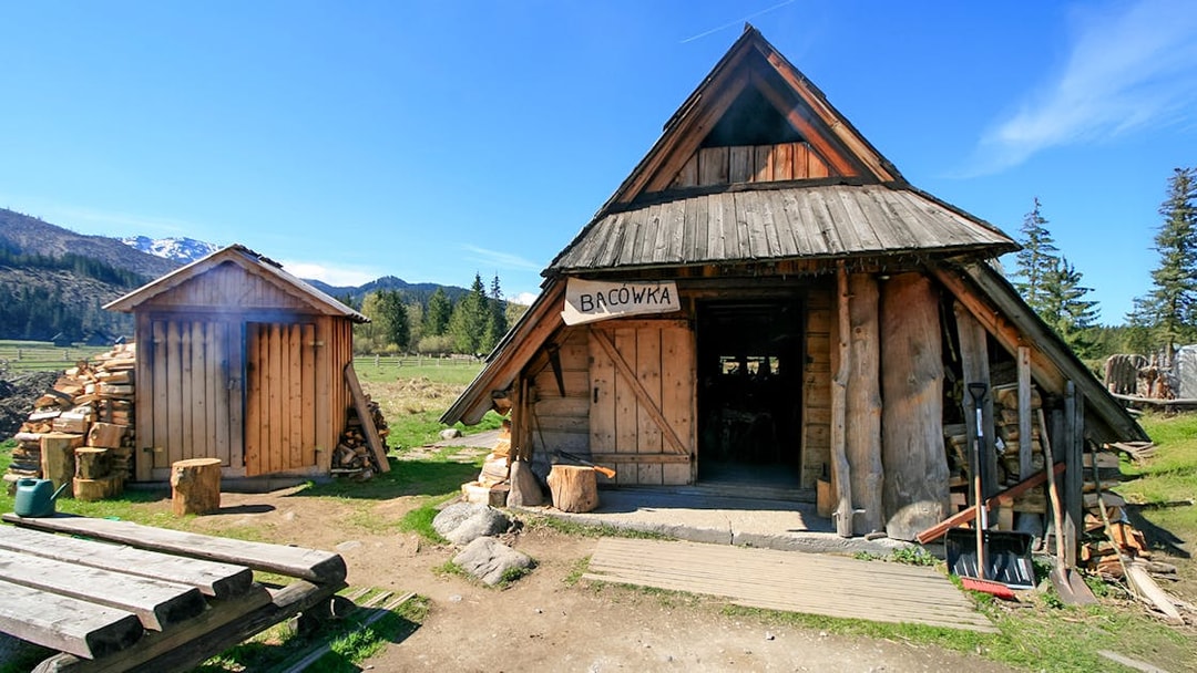 Bacowka Cheese Hut in a mountain meadow with wood stacks and clear sky.