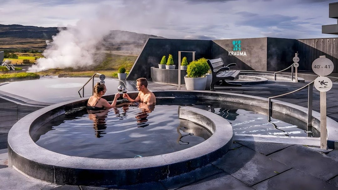 Couple enjoying Krauma Geothermal Baths in Iceland with steam rising in the background.