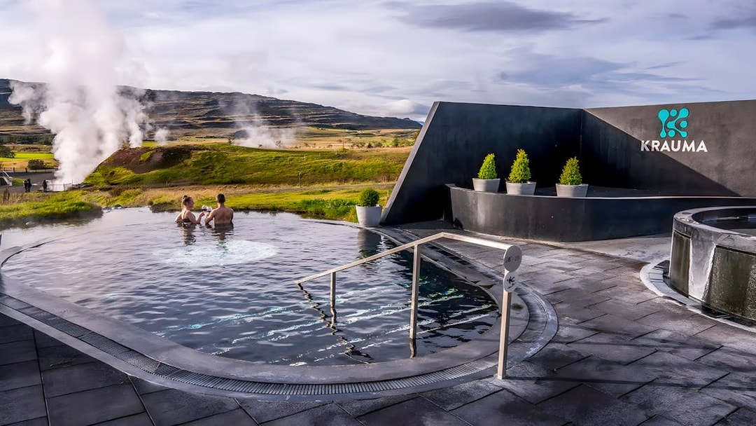 Visitors relaxing in Krauma Geothermal Baths with steam rising in the Icelandic landscape.