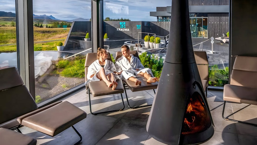 Couple relaxing in robes by a fireplace at Krauma Geothermal Baths, Iceland.
