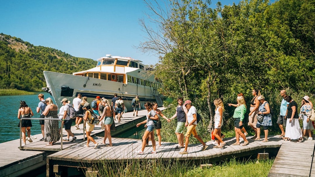 Tourists walking on a wooden path near a boat at Krka National Park.