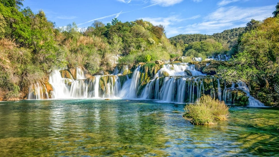 Waterfalls cascading over rocks at Krka National Park, surrounded by lush greenery.