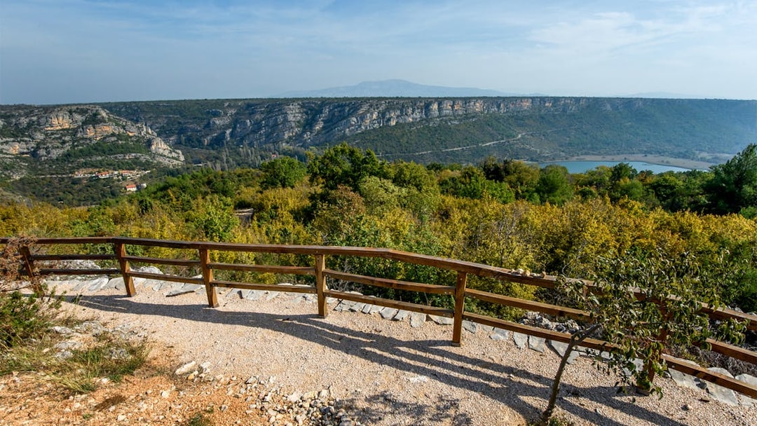 View from a wooden railing at Krka National Park overlooking lush greenery and distant cliffs.