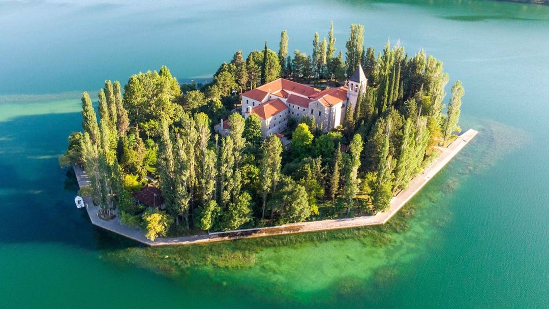 Aerial view of Krka Monastery surrounded by lush trees and turquoise water in Croatia.