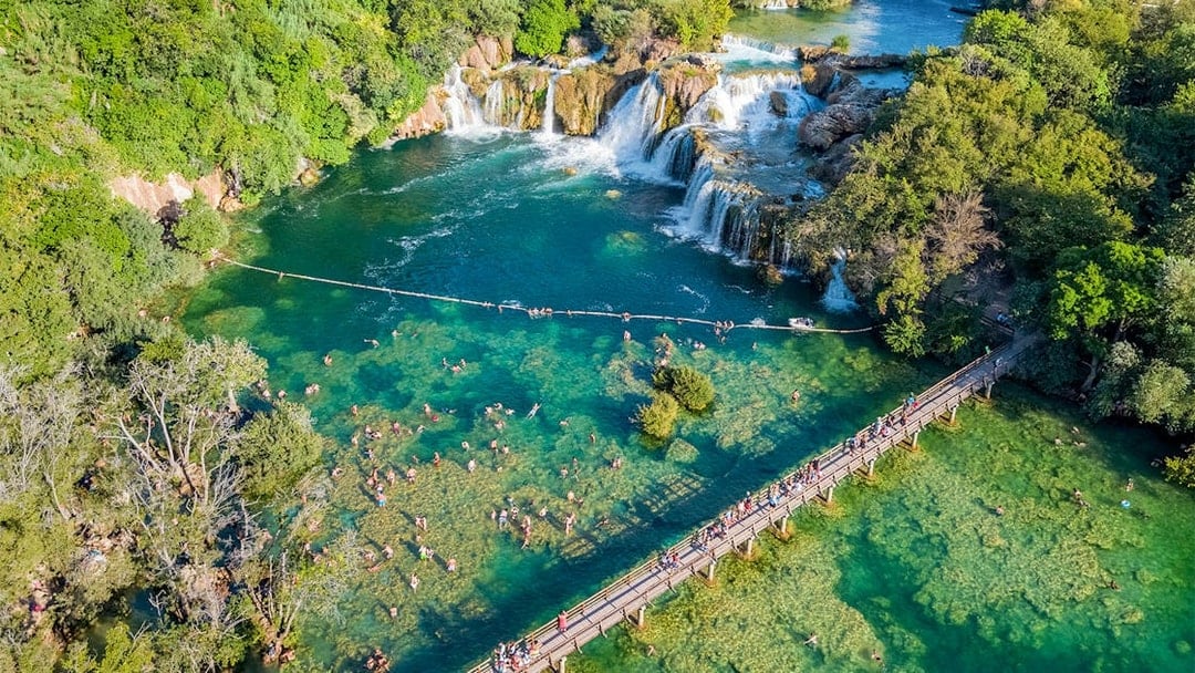 Aerial view of Krka waterfall and bridge with visitors swimming at Krka National Park, Croatia.