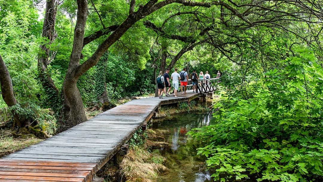 People walking on a wooden path through lush greenery in Krka National Park.