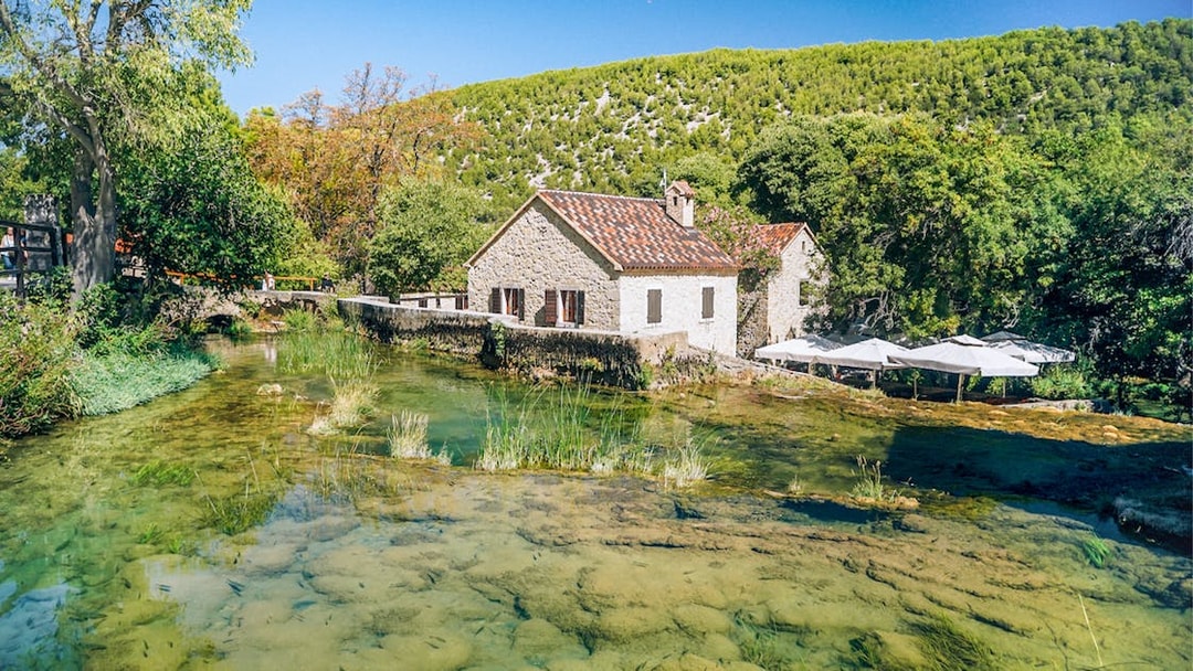 Stone house by a clear stream in Krka National Park, Croatia, surrounded by lush greenery.