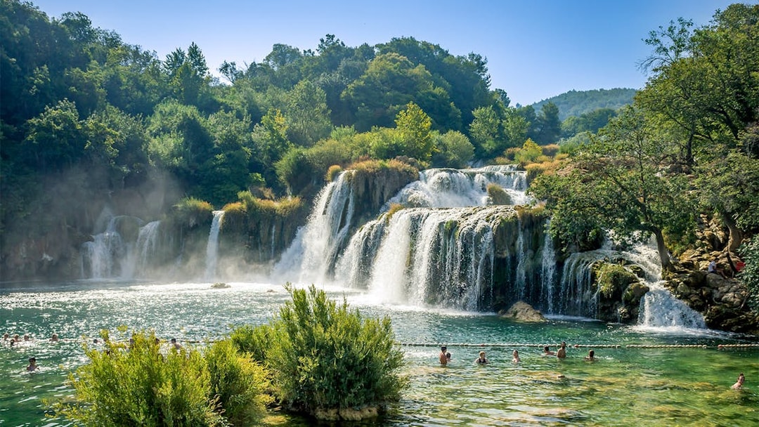 Waterfalls at Krka National Park with people swimming in the foreground.