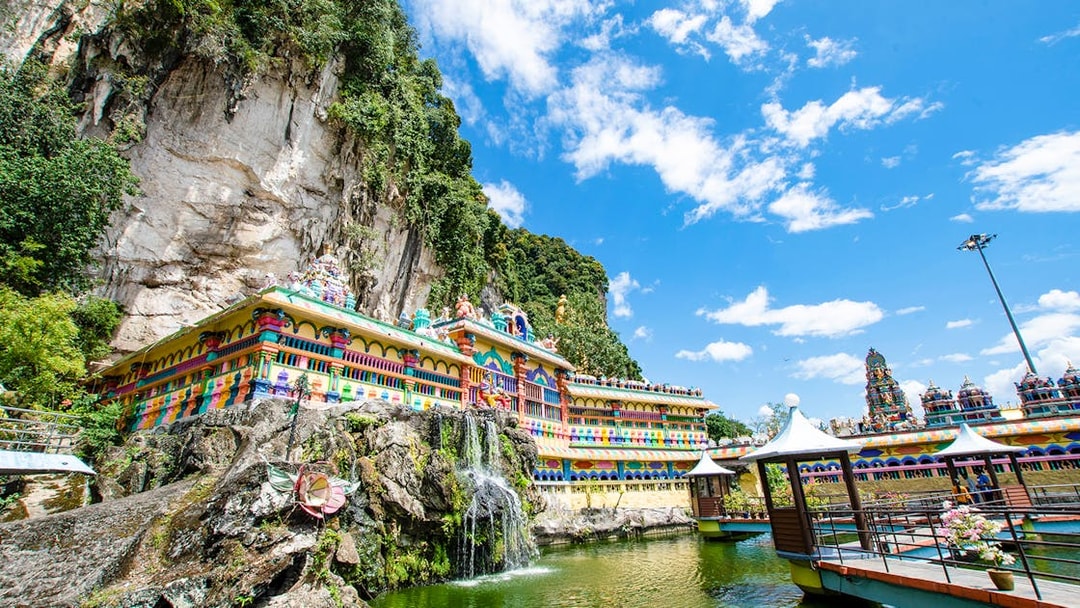 Colorful temple facade at Batu Caves, Kuala Lumpur, with limestone cliffs and blue sky.
