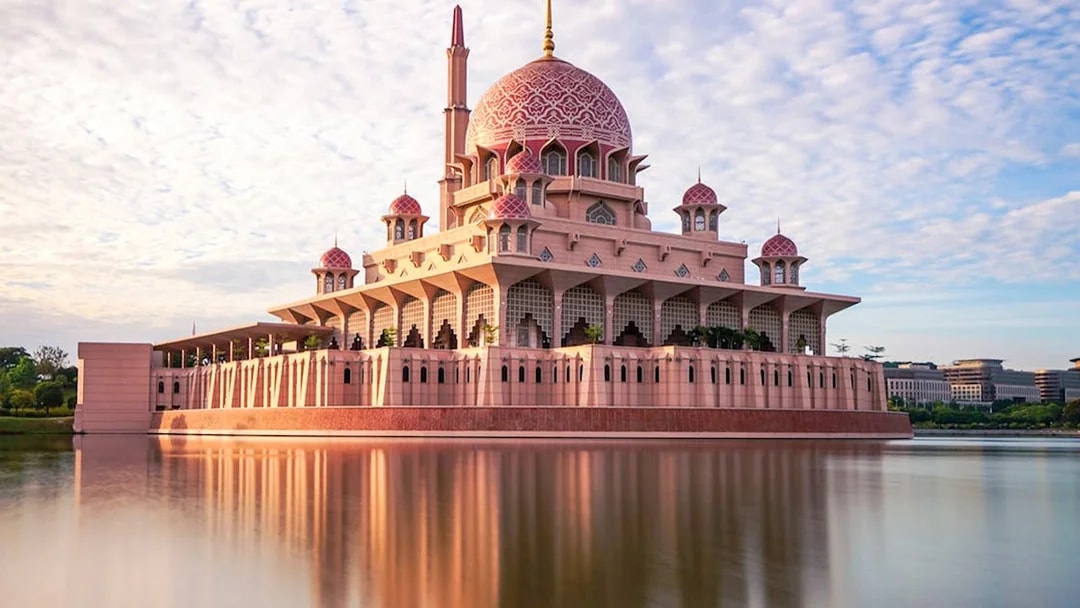 Putra Mosque reflecting in a lake under a blue sky in Kuala Lumpur.