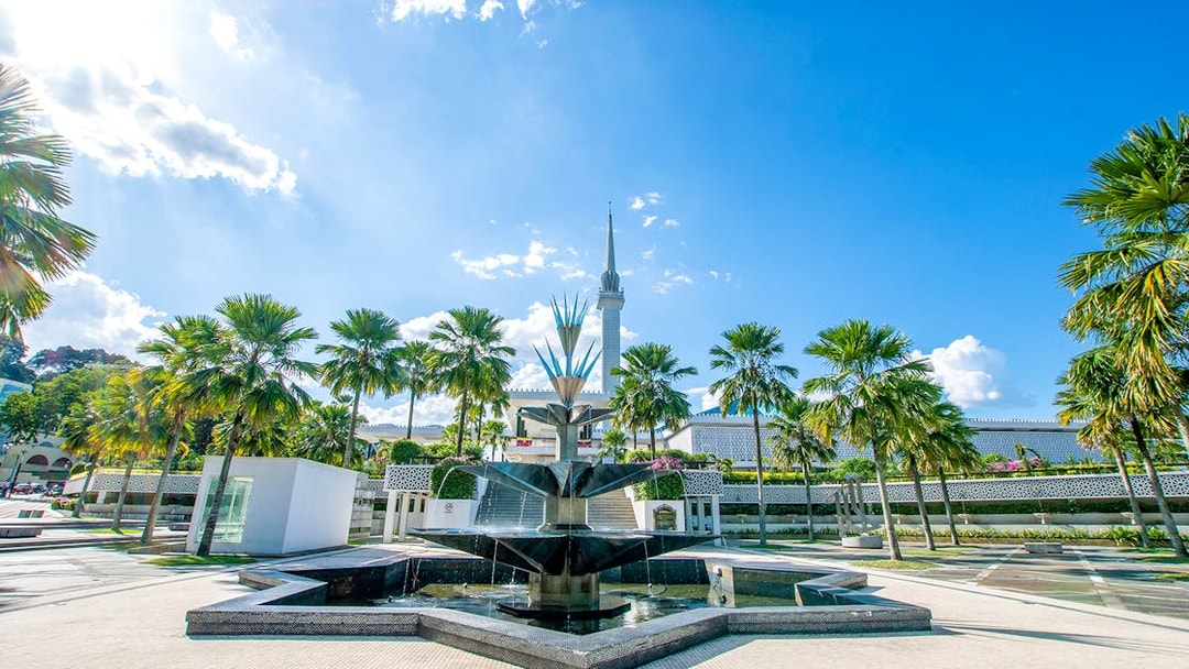 National Mosque of Kuala Lumpur with palm trees and fountain in foreground.