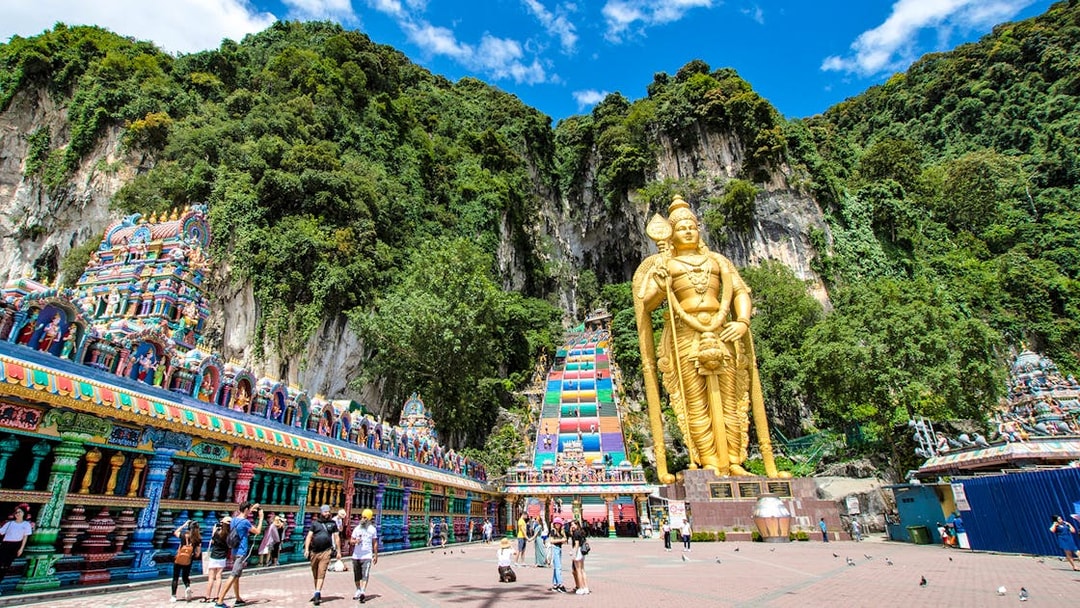 Golden statue of Lord Murugan at Batu Caves entrance, Kuala Lumpur, with colorful temple facade.