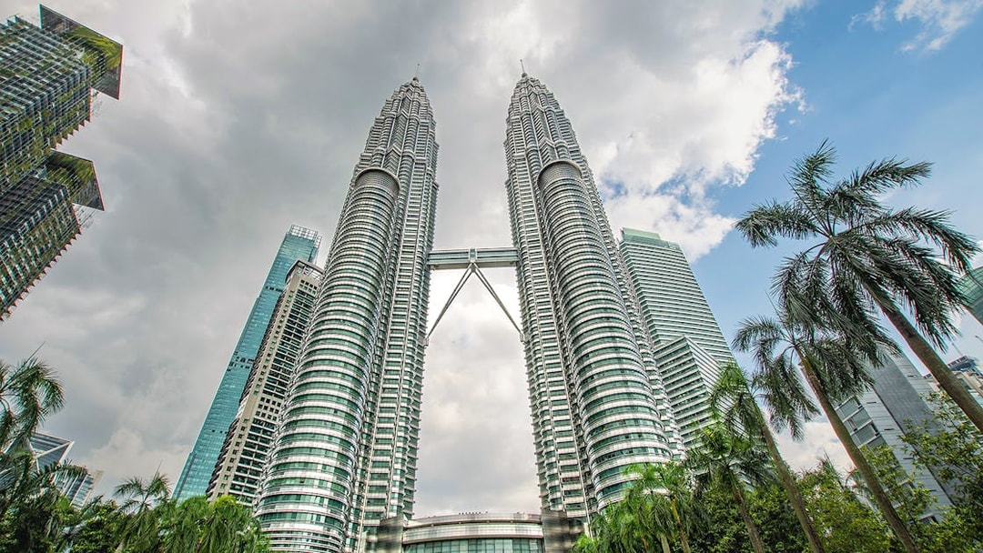 Petronas Twin Towers in Kuala Lumpur with surrounding skyscrapers and palm trees.