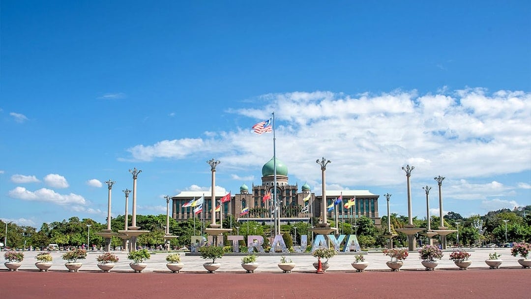 Putrajaya government complex with flags and central dome under blue sky.