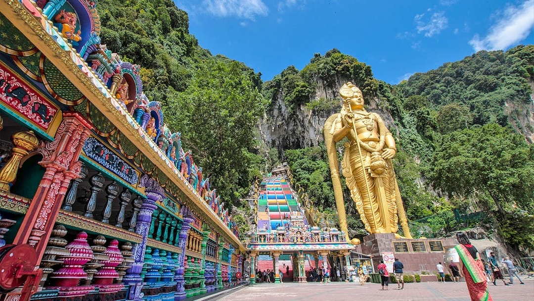 Batu Caves entrance with colorful steps and large golden statue in Kuala Lumpur.