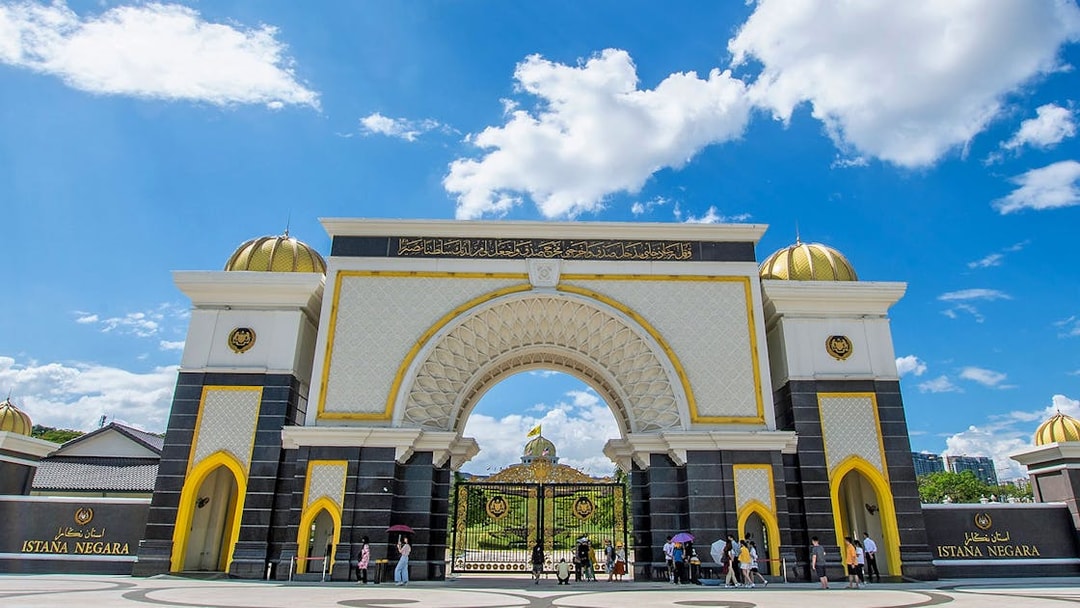 Istana Negara entrance in Kuala Lumpur with visitors and blue sky.