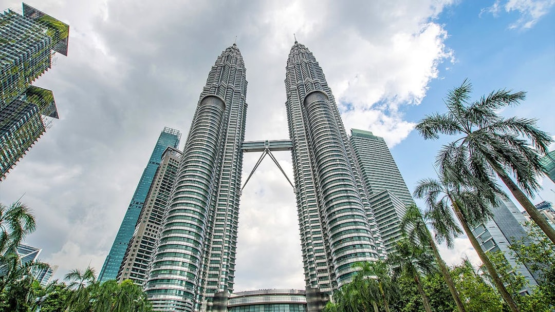 Petronas Twin Towers in Kuala Lumpur with surrounding skyscrapers and palm trees.