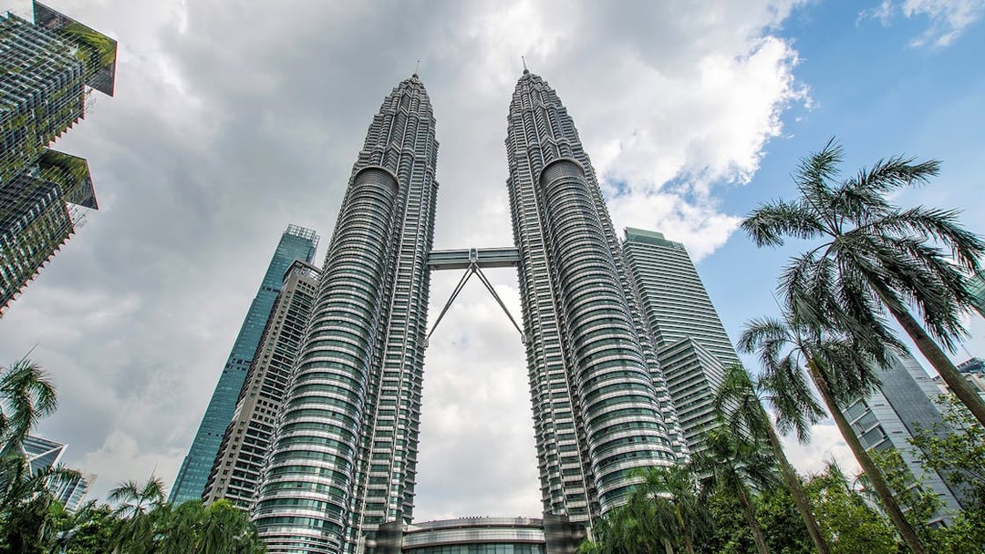 Petronas Twin Towers in Kuala Lumpur with surrounding skyscrapers and palm trees.