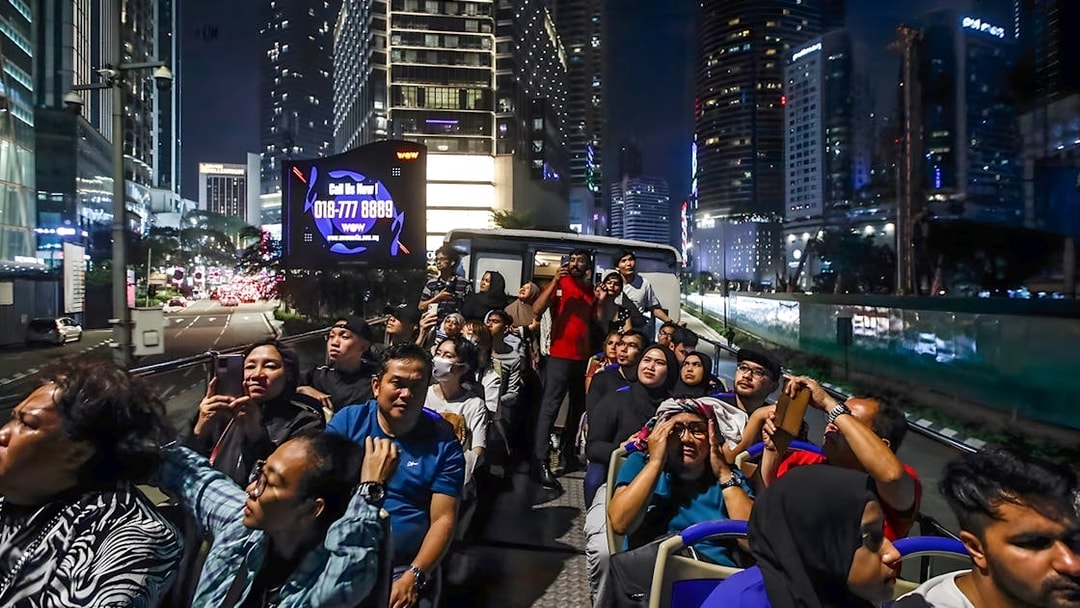 Tourists on Kuala Lumpur night bus tour viewing city skyline.