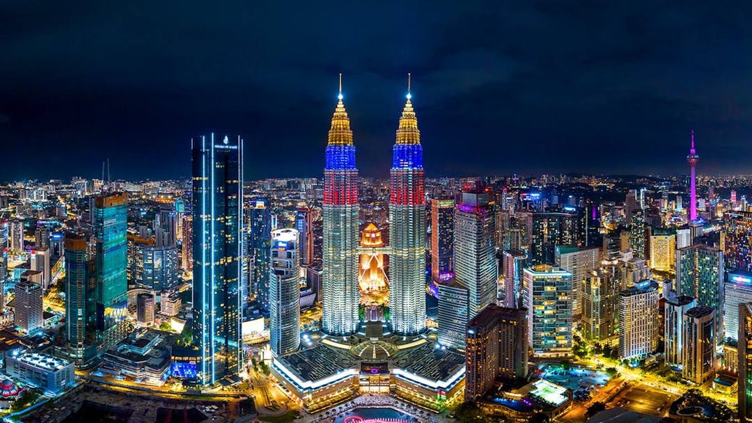 Kuala Lumpur skyline at night featuring the illuminated Petronas Twin Towers.