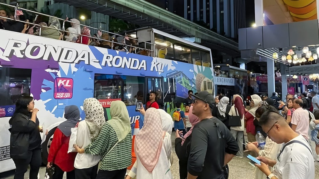 Crowd boarding Kuala Lumpur Hop-On Hop-Off night bus under city lights.