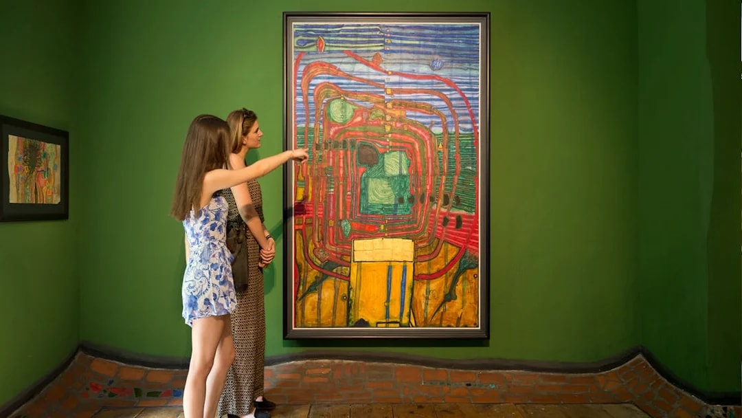 Visitors observing a colorful painting at KUNST HAUS WIEN, Hundertwasser Museum exhibit.