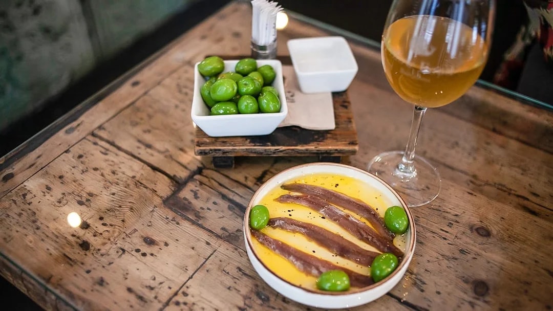 Anchovies and olives on a plate with a glass of wine, La Barceloneta food tour.