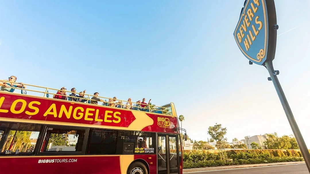 Los Angeles hop-on hop-off tour bus near Beverly Hills sign.