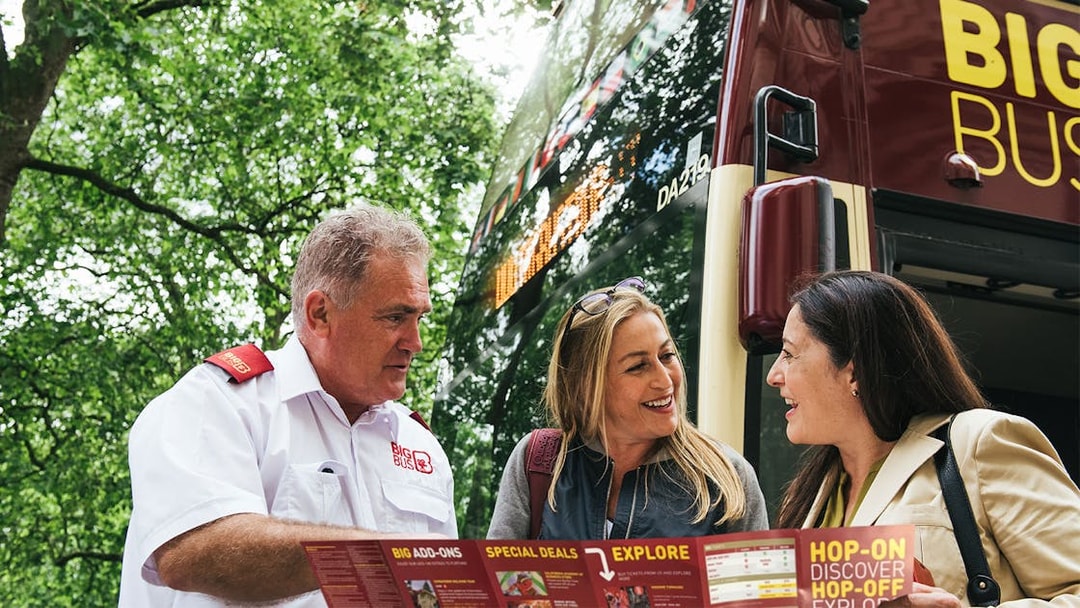 Tourists with a guide in front of a Los Angeles hop-on hop-off bus, holding a map.