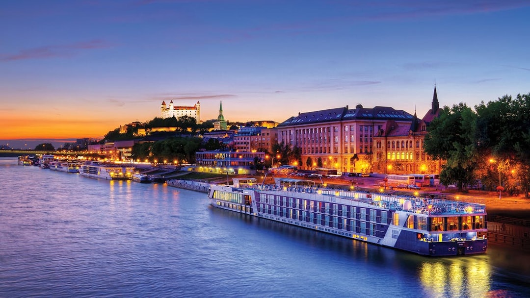 Late evening view of a river cruise ship docked near illuminated buildings in Bratislava.
