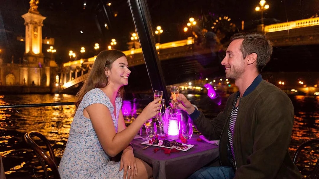 Couple toasting with champagne on a La Marina dinner cruise in Paris at night.