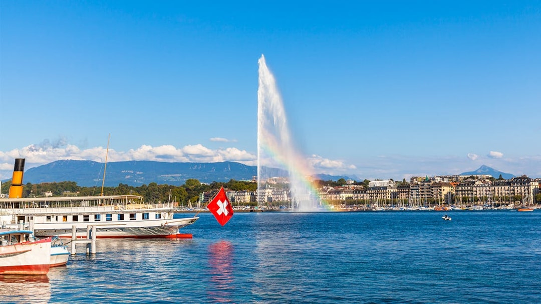 Lake Geneva with Jet d'Eau fountain and Swiss flag boat in the foreground.