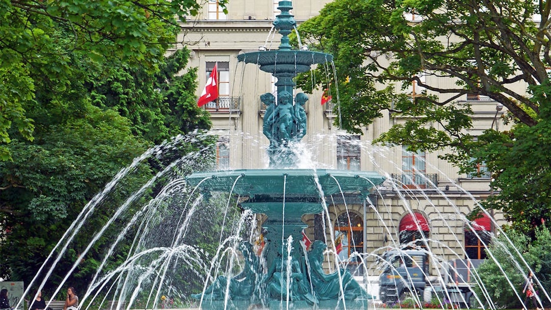 Fountain in front of a historic building with Swiss flags in Geneva.