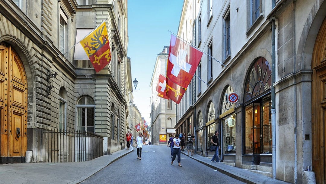 Street in Geneva with Swiss and Geneva flags, part of the Full-Day Guided Tour of Lake Geneva.