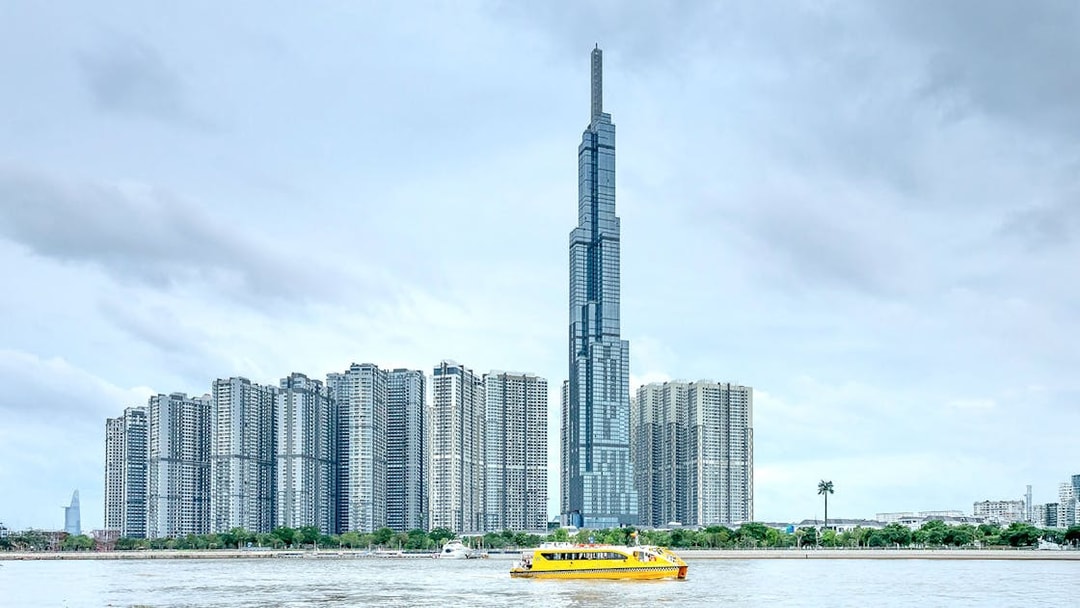 Landmark 81 and nearby skyscrapers by the river with a yellow ferry in Ho Chi Minh City.