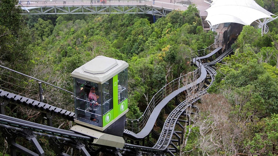 Langkawi SkyGlide ascending through lush forest with SkyBridge in the background.